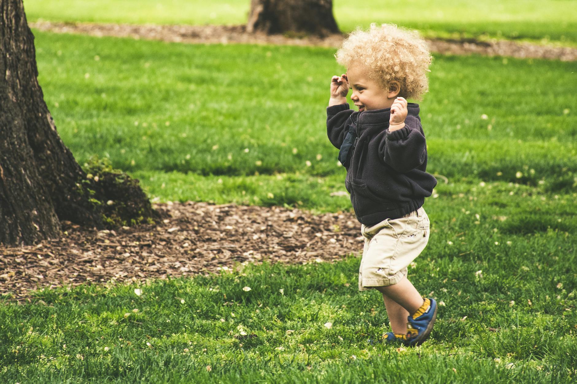 Toddler runs in grass next to tree